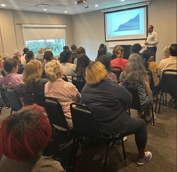 A member presenting a slide to a full room